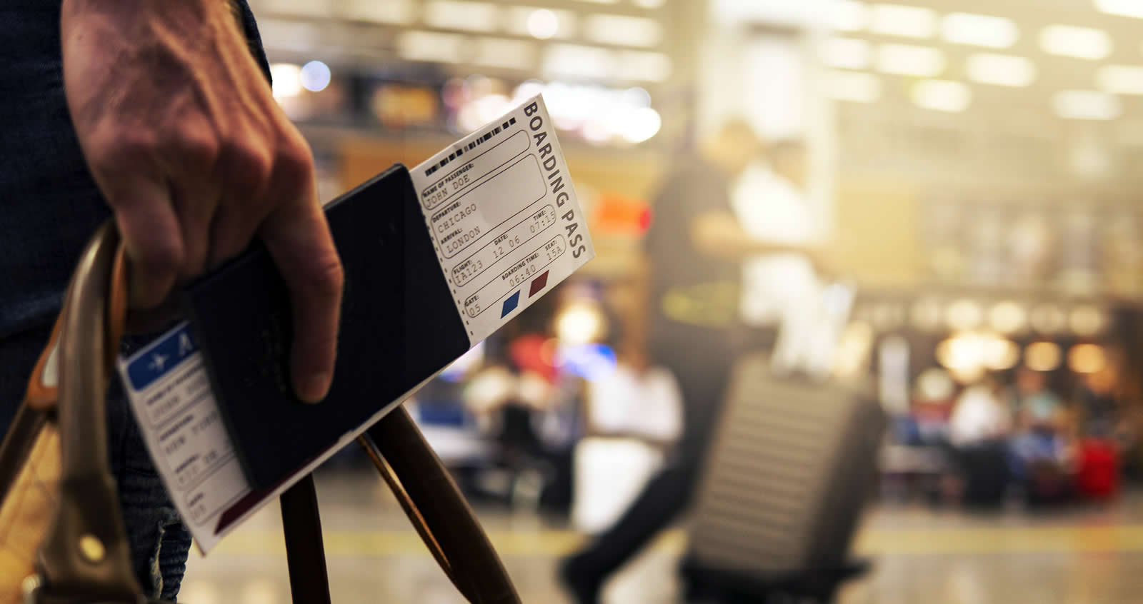 Una mano sosteniendo un pasaporte con la tarjeta de embarque y una maleta de viaje sobre un fondo de sala de aeropuerto